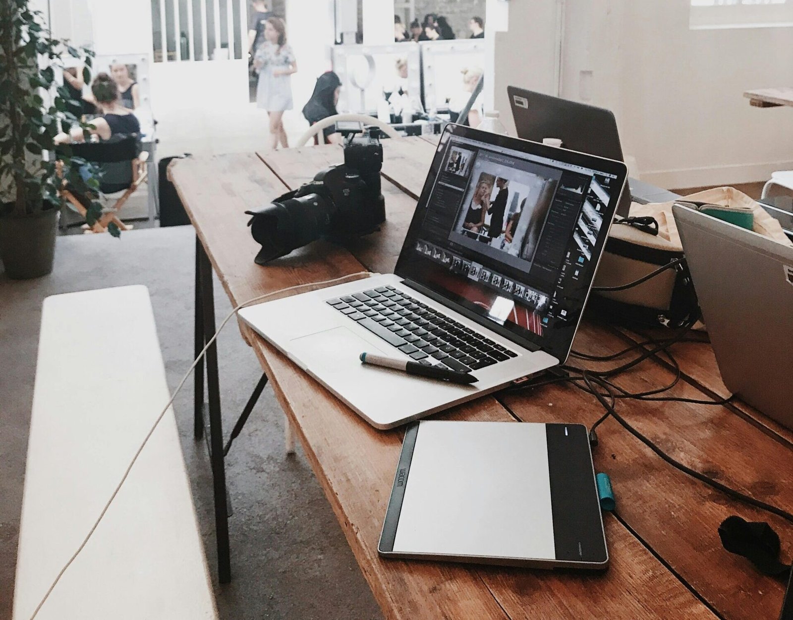 A bright, modern workspace featuring laptops, a camera, and a drawing tablet in an indoor office.